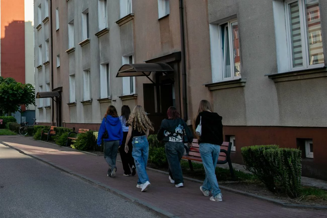 Grupa nastolatek idzie przez osiedle bloków.