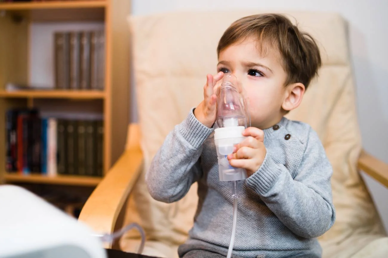 Małe dziecko z nebulizatorem podczas inhalacji z powodu duszącego kaszlu.