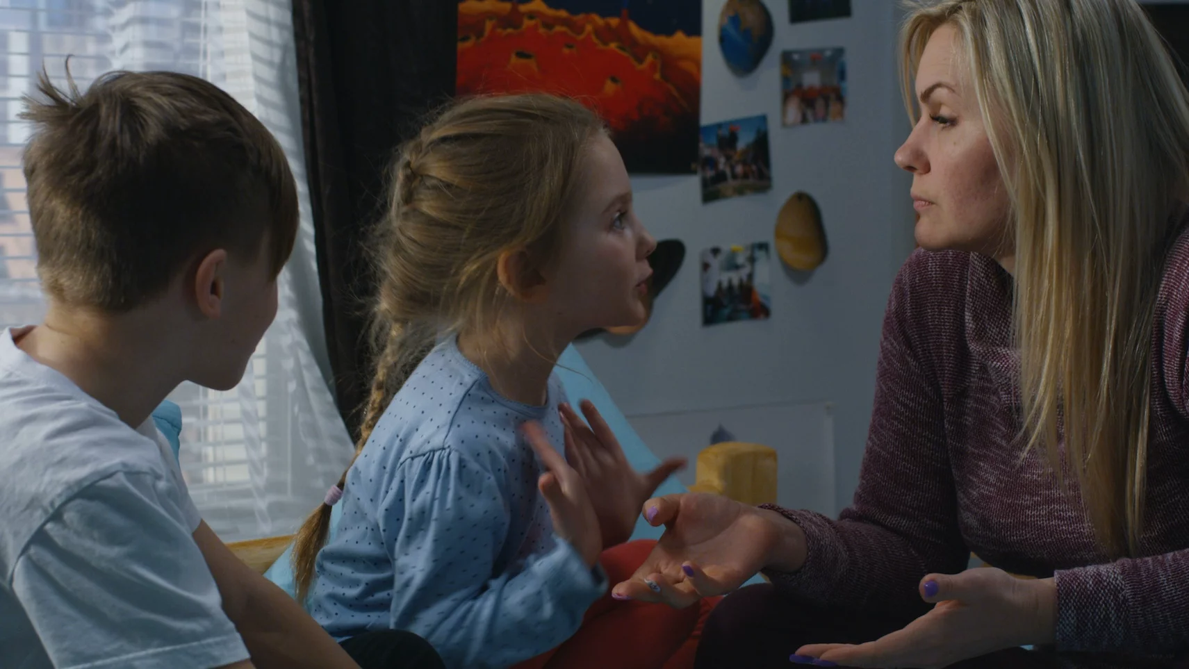 Czy ingerować, kiedy dzieci się kłócą? Na zdjęciu mama i dwójka dzieci siedzą na łóżku - dzieci są w trakcie kłótni, mama próbuje rozwiązać ich problem.