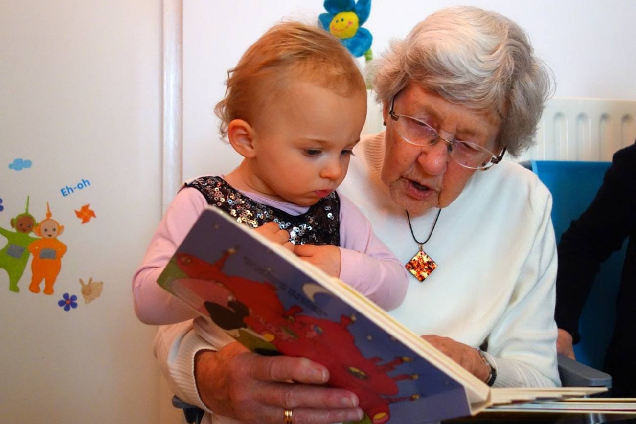 Babcia zajmuje się wnuczką i czyta jej książkę.