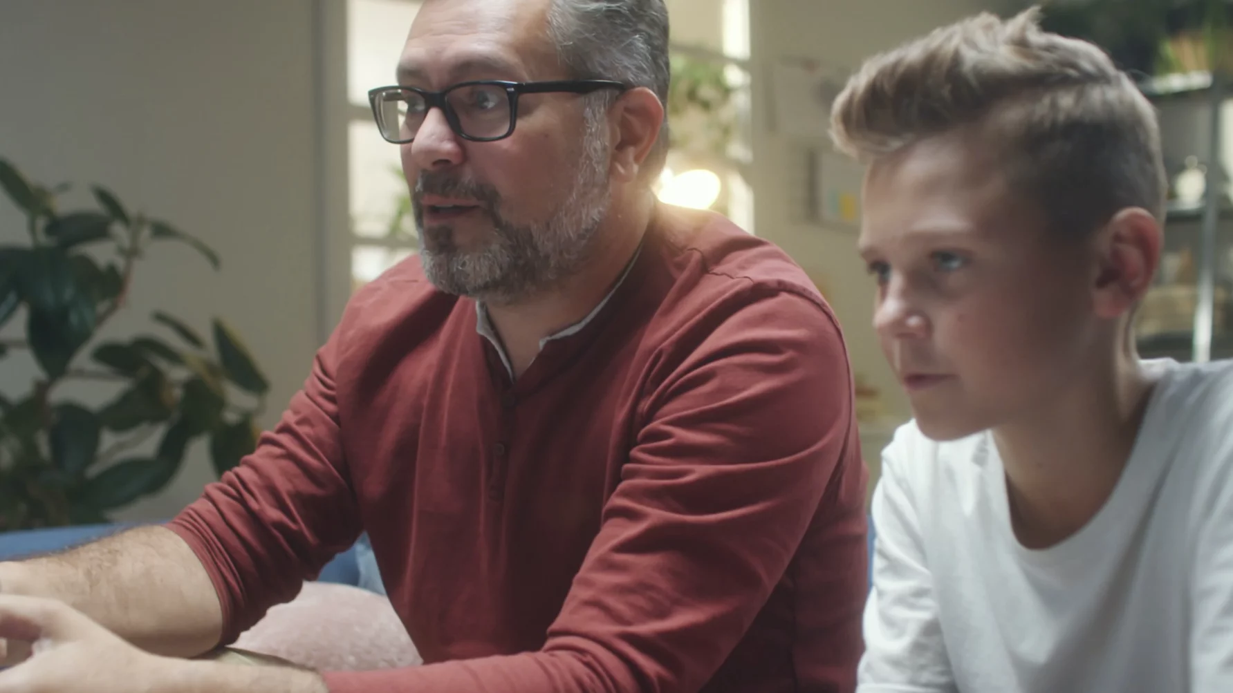 Tata siedzi z synem na kanapie. Grają i rozmawiają.