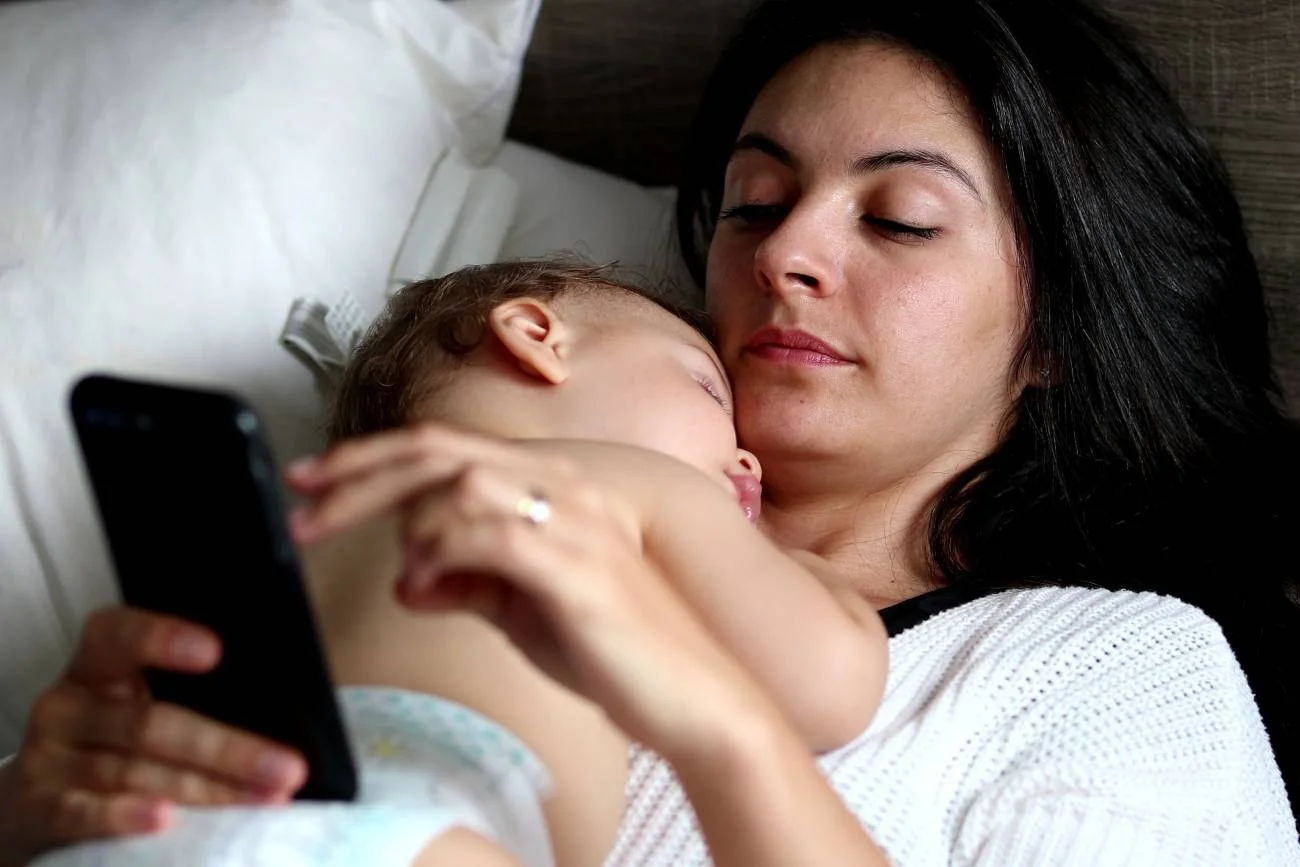 młoda mama czyta komentarze o macierzyństwie na smartfonie