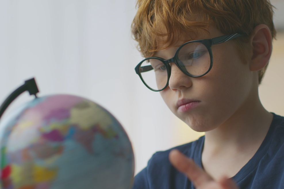 Na zdjęciu widać chłopca, który patrzy na globus
