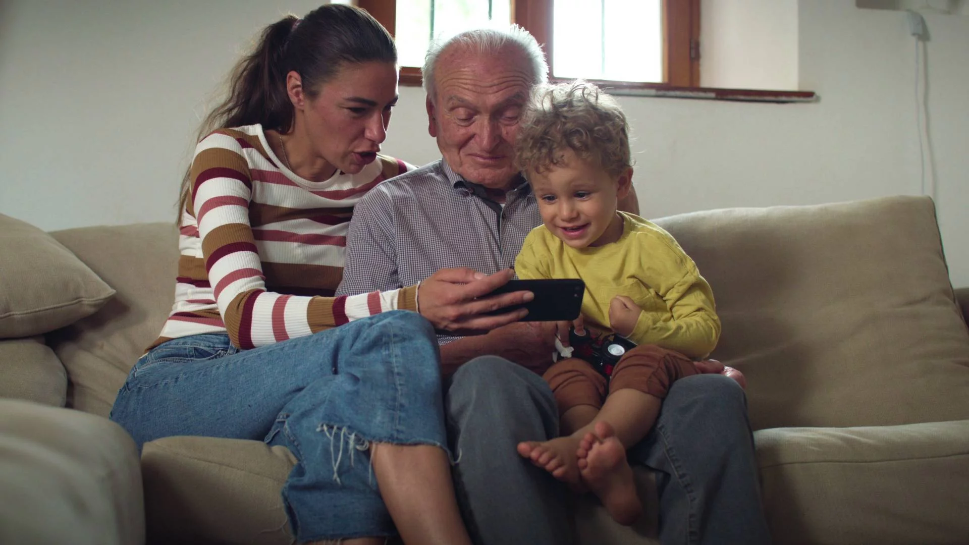 chłopiec siedzi z dziadkiem i mamą na kanapie i ogląda coś na smartfonie chłopiec siedzi z dziadkiem i mamą na kanapie i ogląda coś na smartfonie