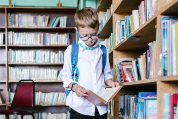 Chłopiec stoi w bibliotece i przegląda książkę.