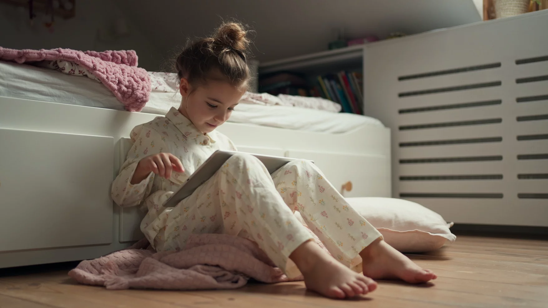 Na zdjęciu dziewczynka siedzi przy łóżku, czyta książkę i szykuje się do snu,