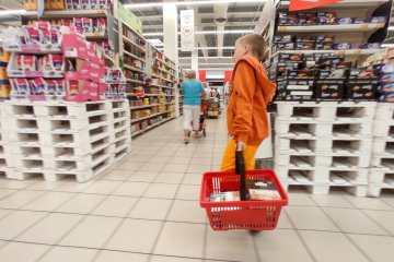 Mały chłopiec robi zakupy, idzie z koszykiem w sklepie.