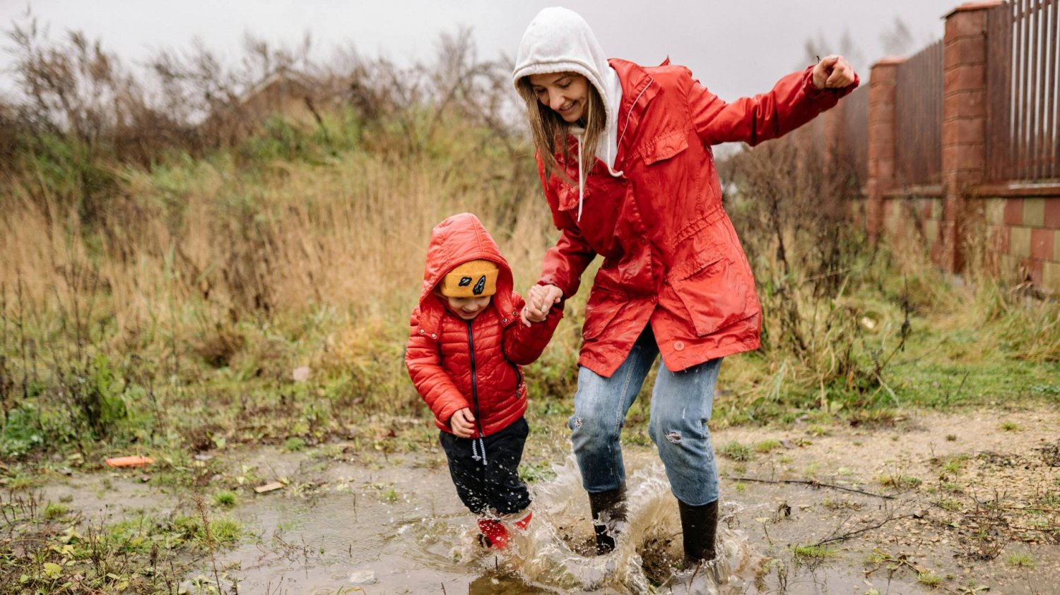 mama z dzieckiem bawi się i skacze po kałużach mama z dzieckiem bawi się i skacze po kałużach