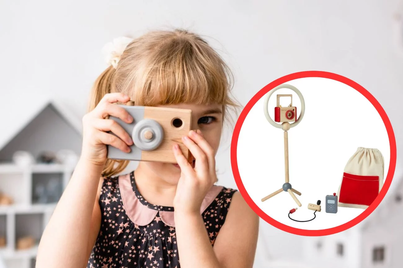 Dziewczynka bawi się drewnianym aparatem fotograficznym.