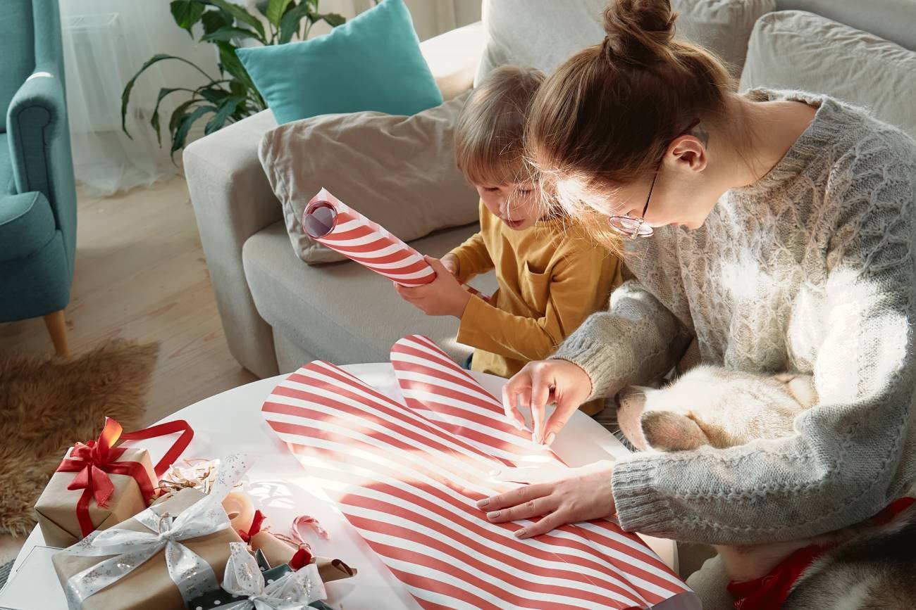 Mama z synkiem pakują świąteczne prezenty w papier.