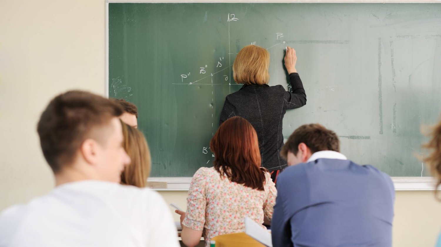 nauczycielka pisze na tablicy przed klasą nastolatków
