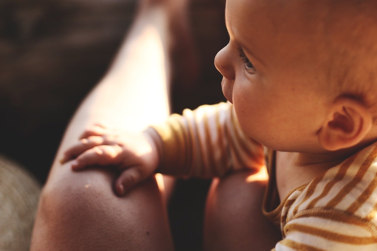 Niemowlę trzyma rączki na kolanach kobiety.