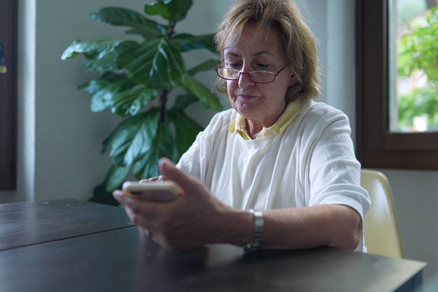 babcia patrzy na ekran smartfona, siedząc przy stole