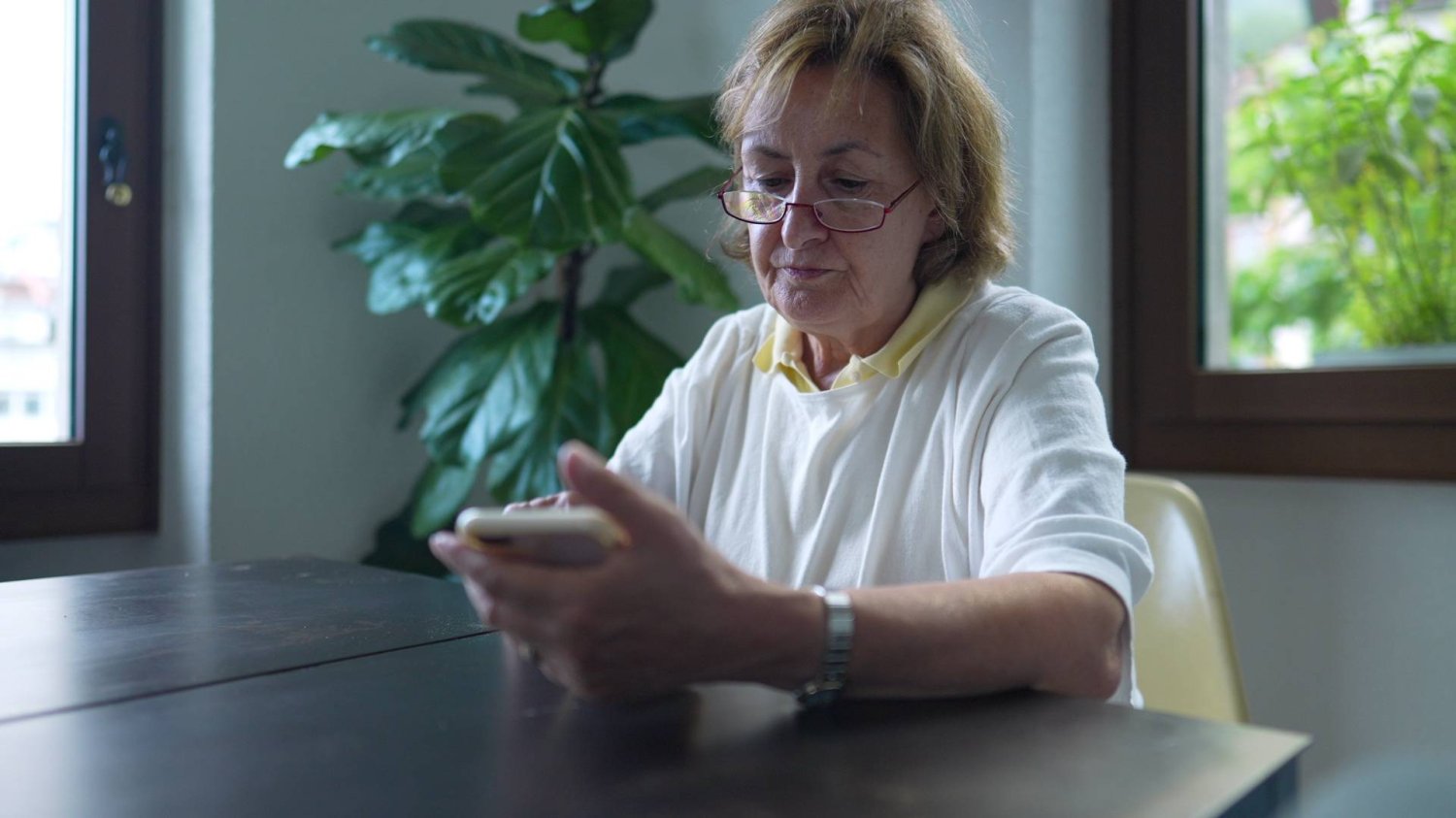 babcia patrzy na ekran smartfona, siedząc przy stole babcia patrzy na ekran smartfona, siedząc przy stole