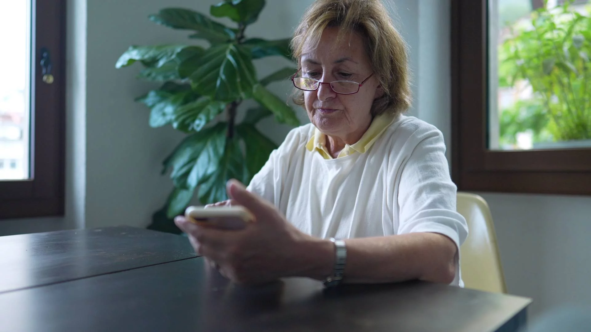 babcia patrzy na ekran smartfona, siedząc przy stole