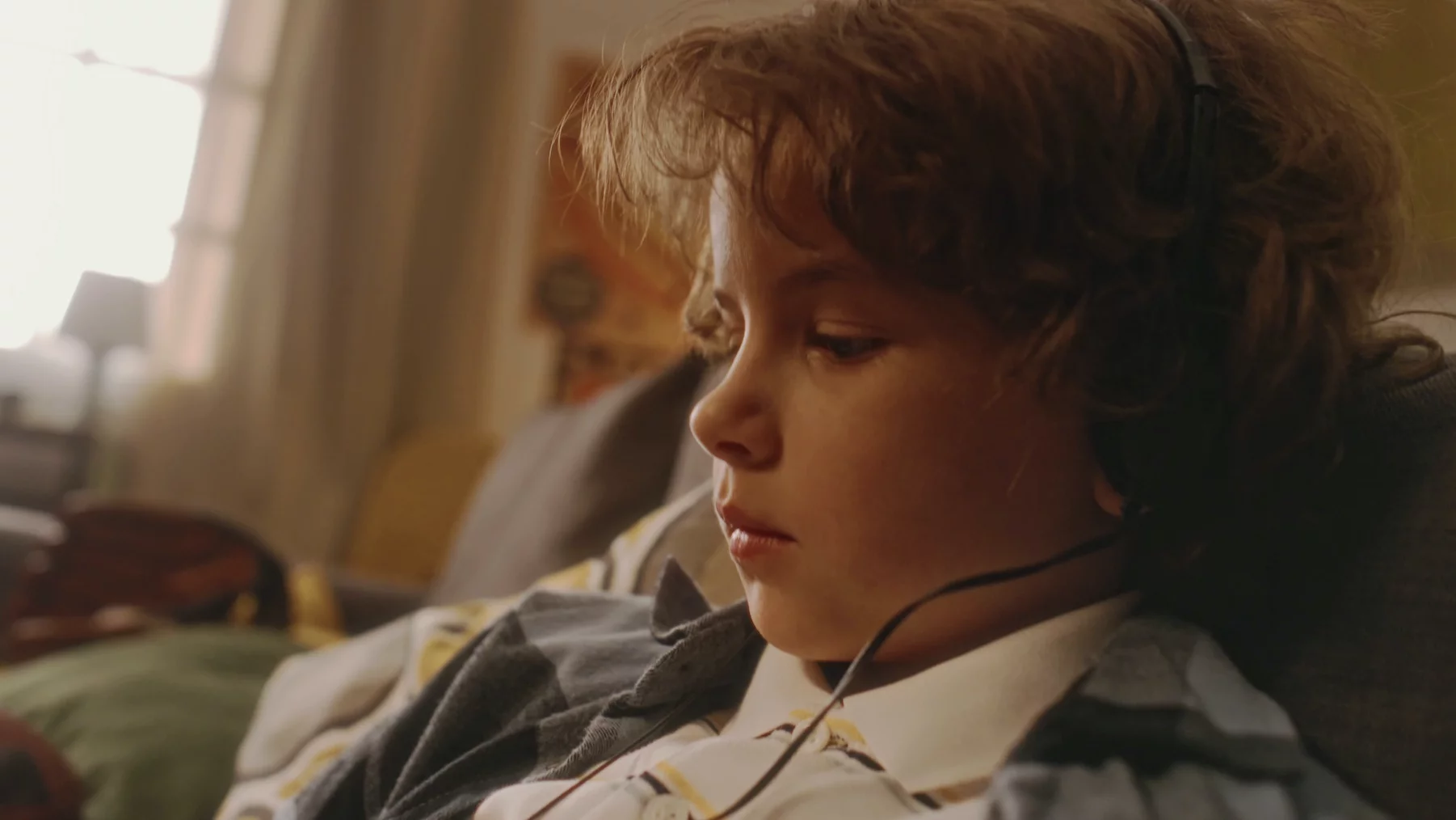 To, co słyszeliśmy od rodziców, wpływa na nasze dorosłe życie Na zdjęciu smutny chłopiec siedzi na kanapie i słucha czegoś na słuchawkach