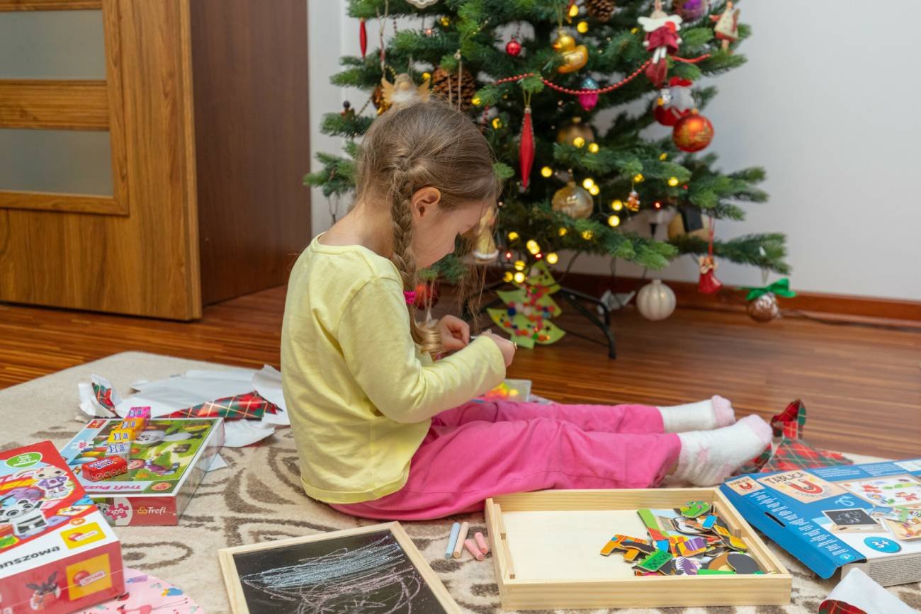 Dziewczynka obok choinki rozpakowuje prezenty.