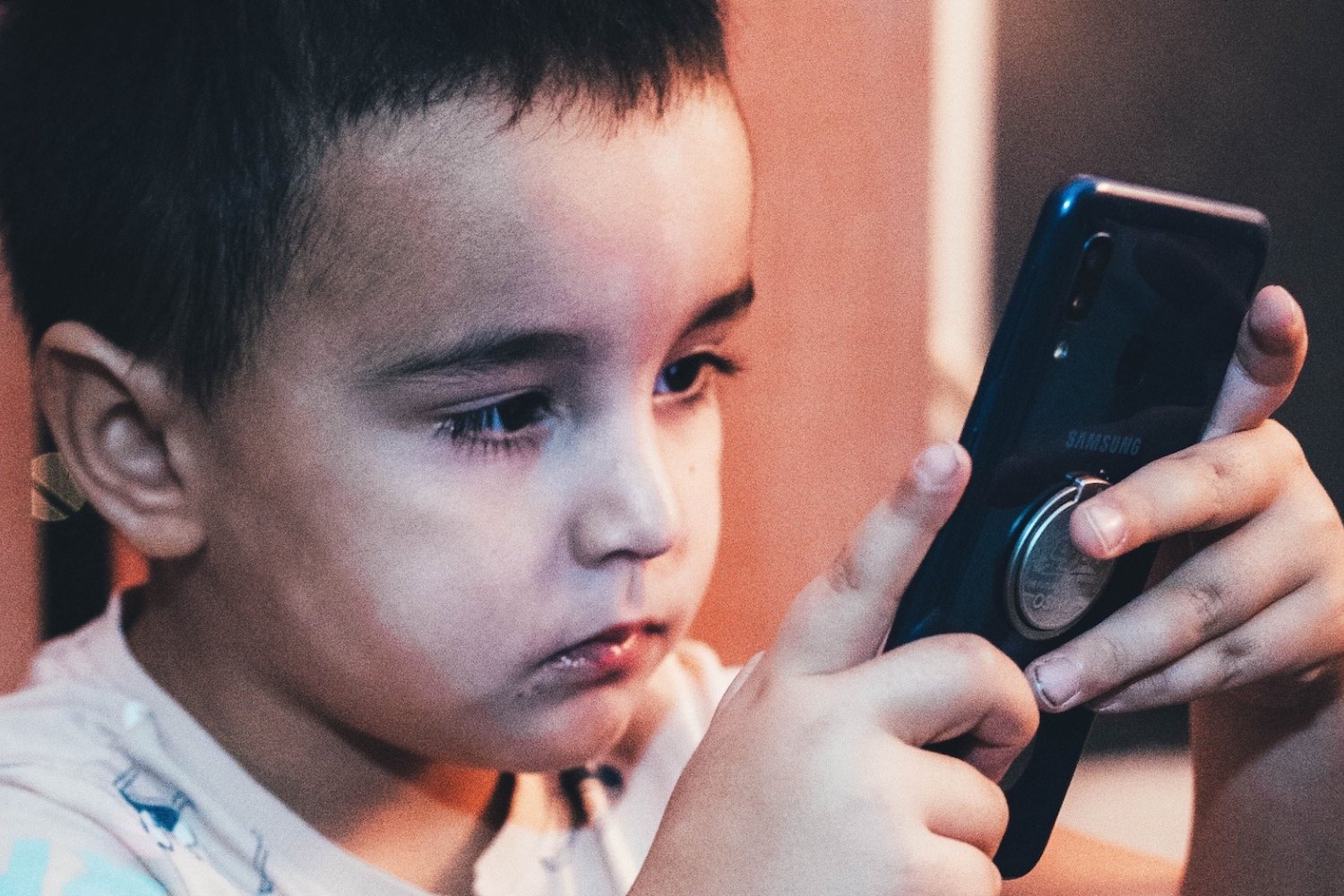 Na zdjęciu chłopiec wpatrzony w telefon.