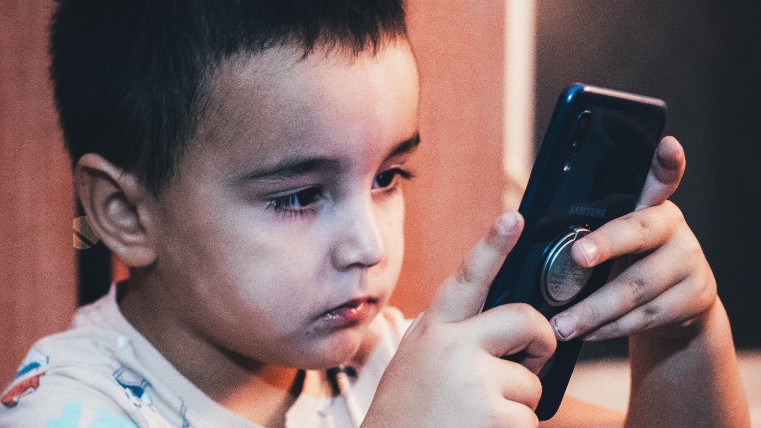 Na zdjęciu chłopiec wpatrzony w telefon.