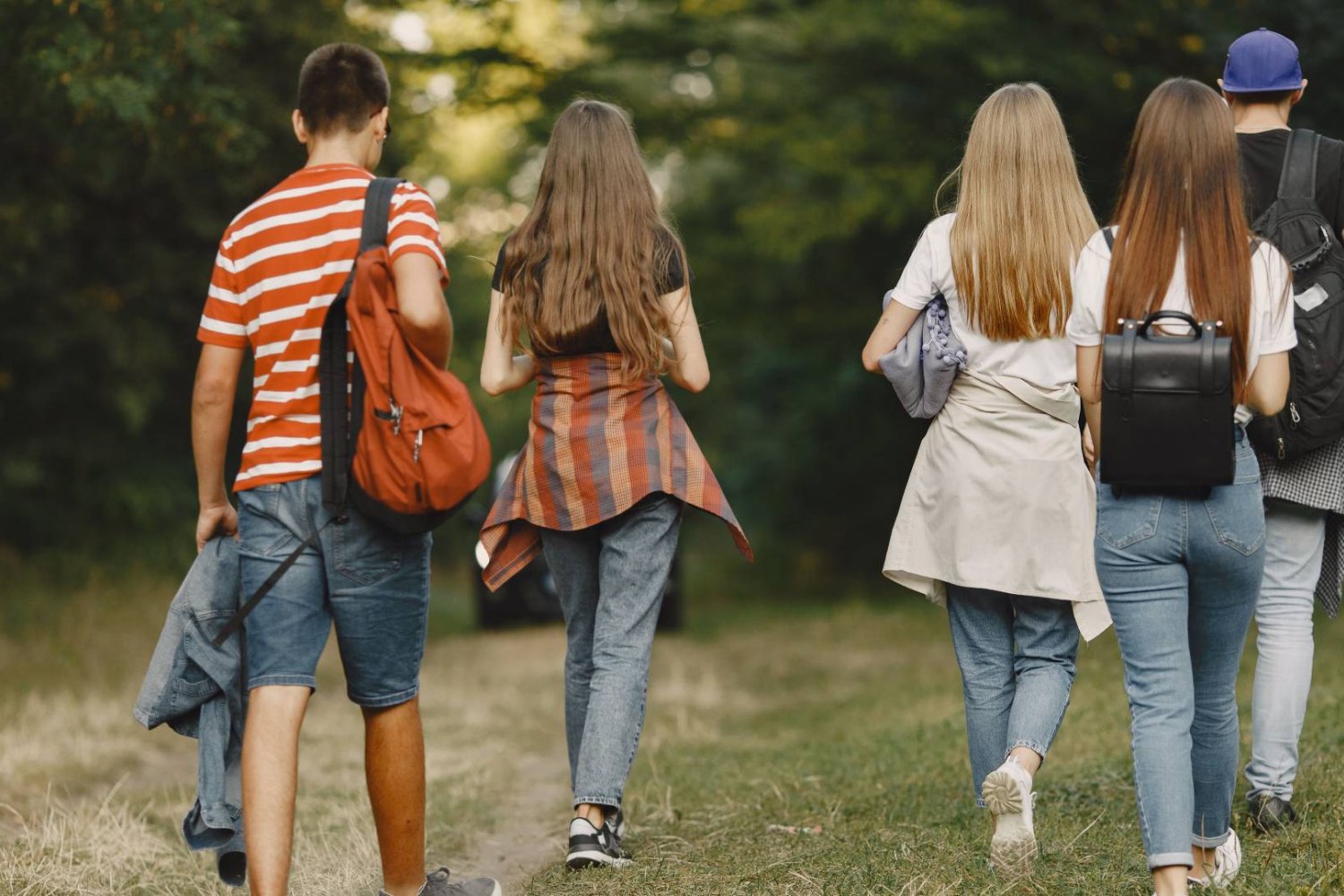 uczniowie z plecakami idą przez park