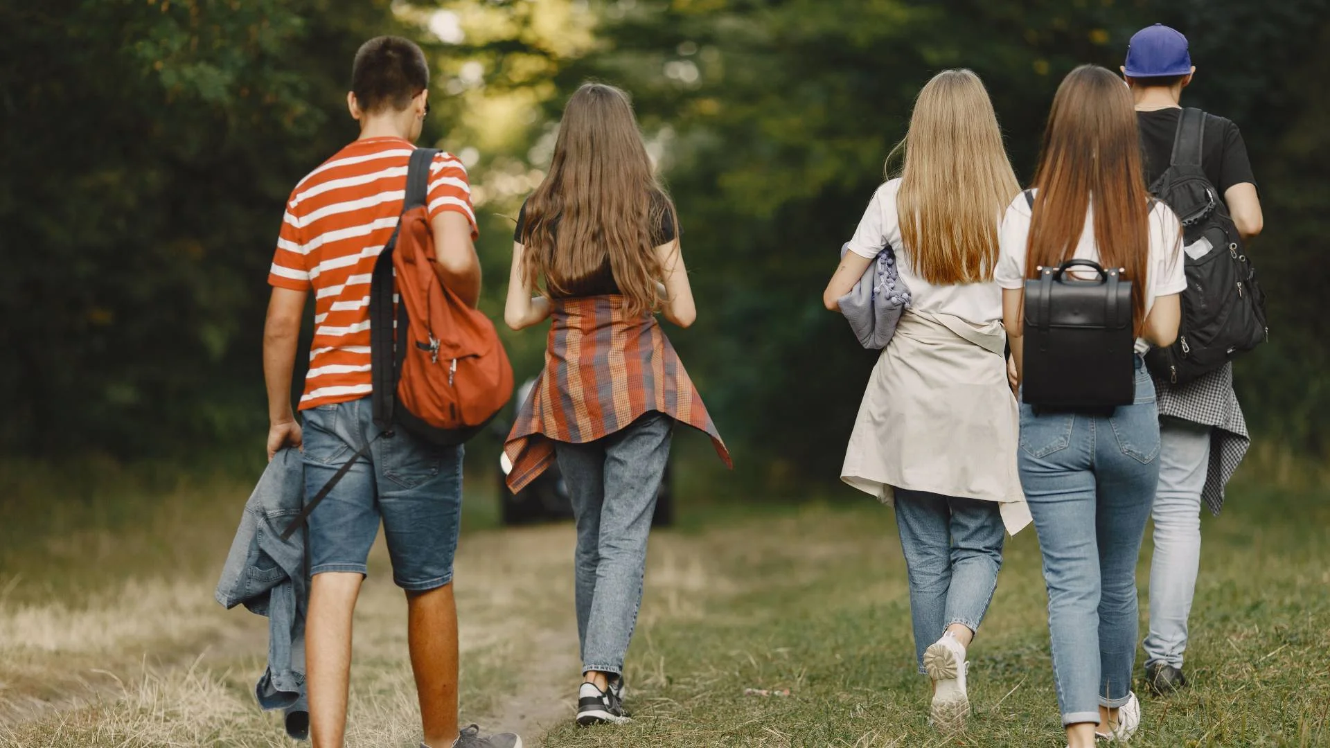 uczniowie z plecakami idą przez park